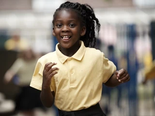 Happy primary pupil running through a playground.
