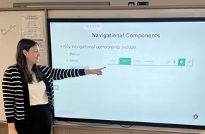 Sarah, a computing teacher, pointing to a navigation bar on a smartboard during a classroom lesson.